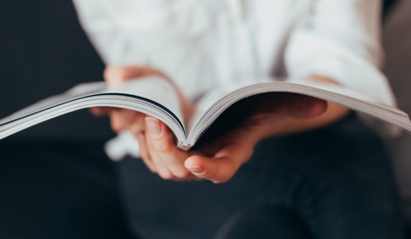 Beautiful female hands hold an open book or magazine in a room on a black sofa